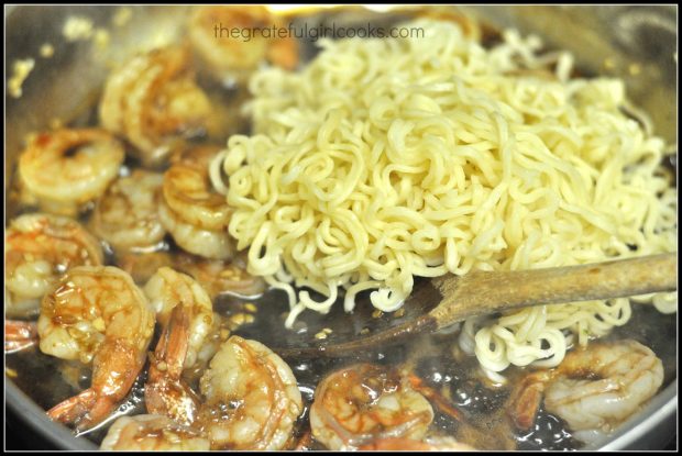 Ramen noodles are added to the cooked shrimp in the skillet.