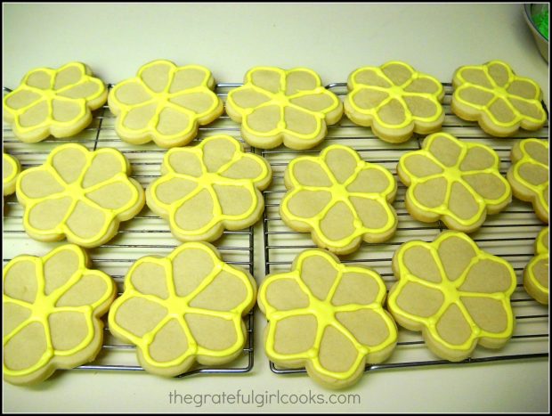 Yellow Royal icing is piped on edges of Spring flower sugar cookies on rack.