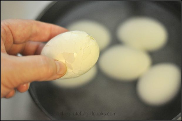 Hand holding a cracked hard boiled egg over saucepan