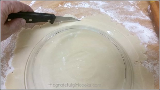 Cutting the pie crust out with a knife using an inverted pie pan for measuring.