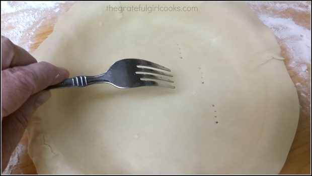 Pricking an unbaked quiche crust with the tines of a fork, before baking.