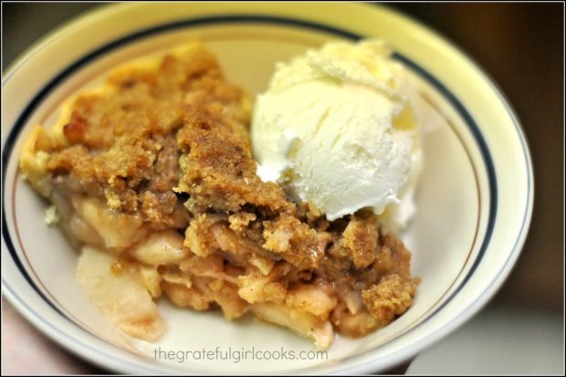 A slice of Dutch crumb apple pie, served with a scoop of vanilla ice cream.