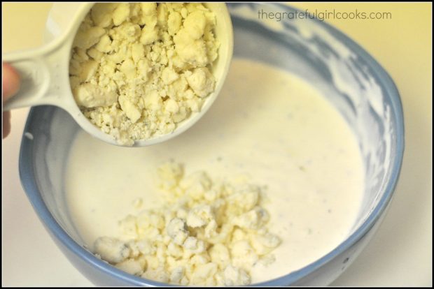 Bleu cheese crumbles are added to the homemade salad dressing in bowl.