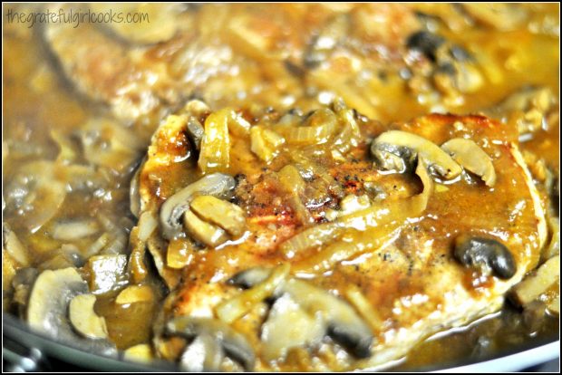 Pork chops with mushroom and onion gravy cooking in skillet.