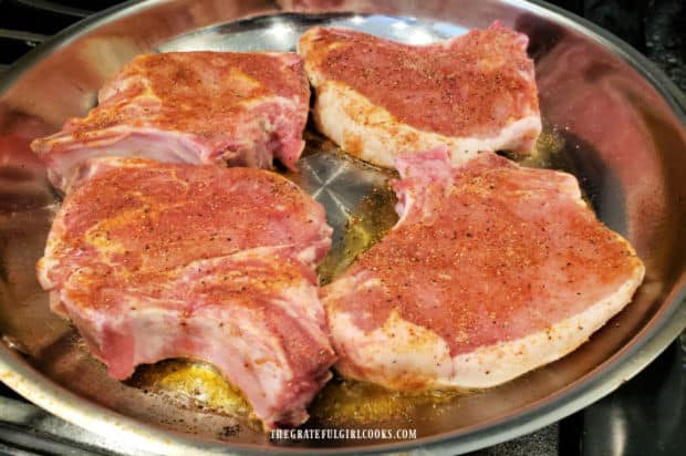 Bone-in pork chops are being pan-seared in a large skillet.