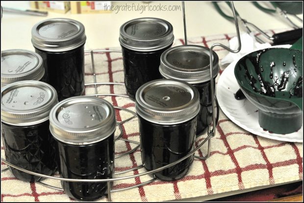 Filled jars of blueberry preserves are placed onto canning rack