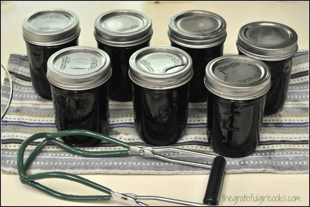 Jars of blueberry jam are sealed and cooling down on dish towel