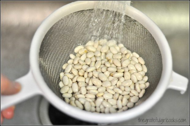 White colander with beans being rinsed in water