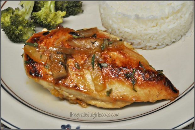 A piece of sticky orange chicken is served with rice and broccoli on the side,.