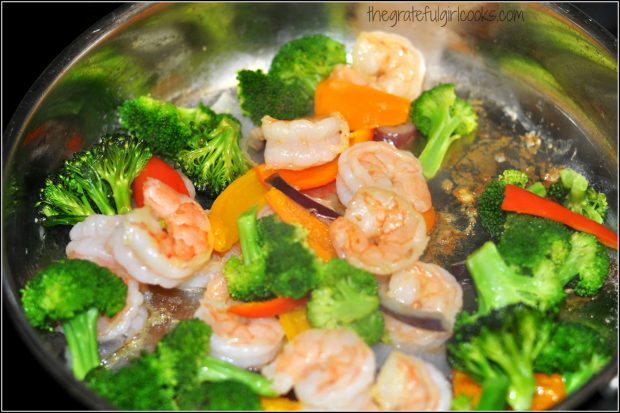 Steamed veggies are added to the skillet of cooked shrimp.