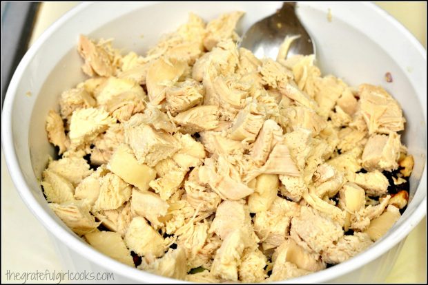 Cooked chicken breast chunks added to salad ingredients in bowl.