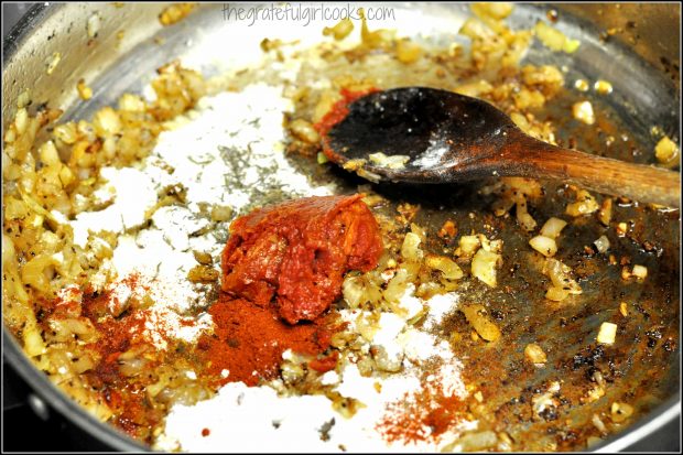 Spices and tomato paste added to cooked onions in skillet to make pork paprikash sauce.