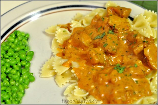 Pork paprikash and noodles on a plate with peas.