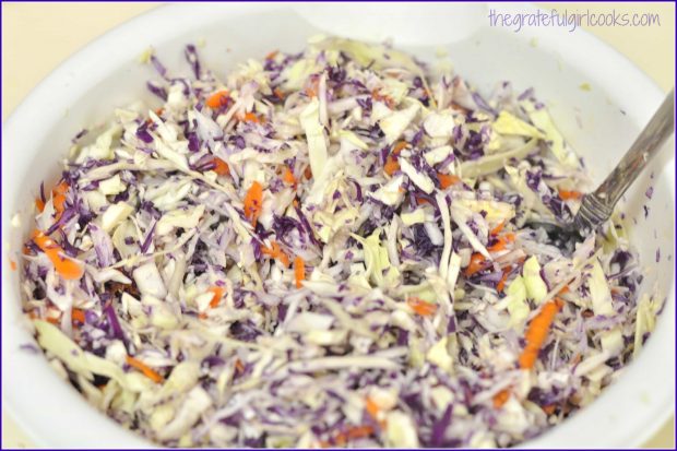 Green and purple cabbage, plus carrot shreds are mixed together in large bowl.