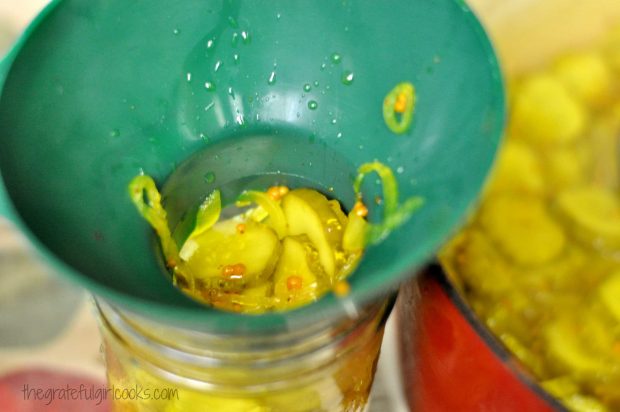 Adding cucumber mixture for pickles to canning jar with a green funnel