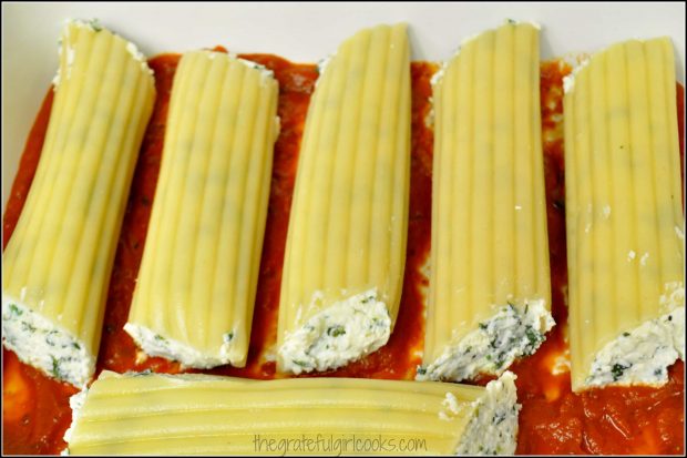 Stuffed florentine manicotti are laid on top of sauce in baking dish.