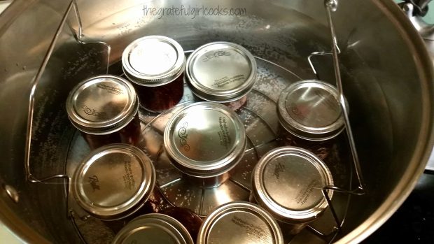Jars of raspberry jam sit in water on rack inside canner