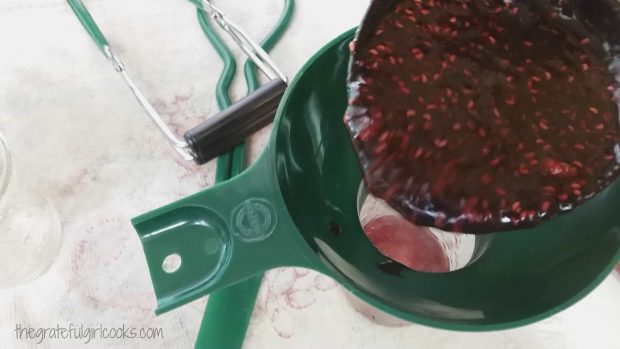 Hot raspberry jam is ladled into hot canning jars using a funnel