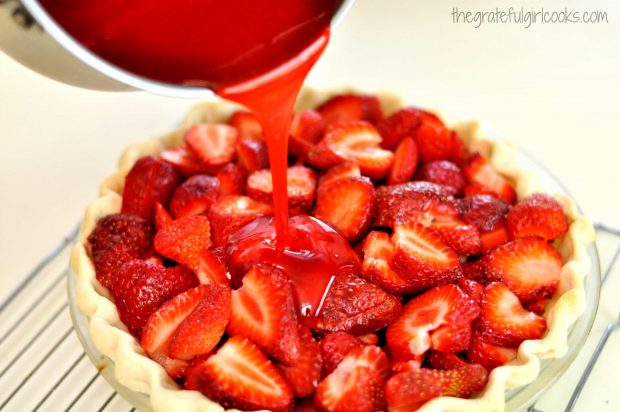 Strawberry glaze is poured over strawberry pie in crust.