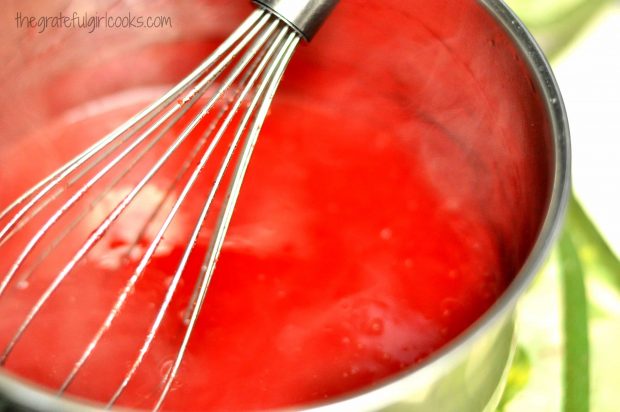 Strawberry pie filling in saucepan with metal whisk.