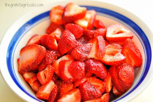 Fresh strawberries, sliced in bowl with blue rim, ready to go into a pie crust.