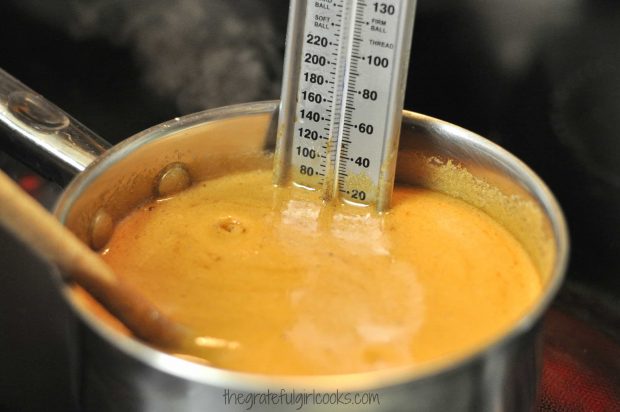 Candy thermometer in saucepan full of bacon pecan pralines sauce.