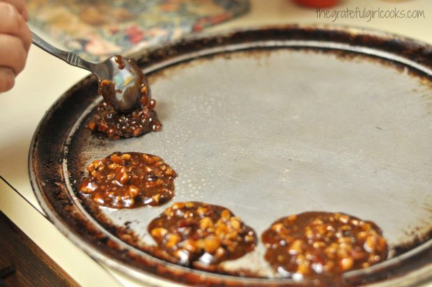 Dropping spoonfuls of bacon pecan pralines onto round baking pan, to cool.