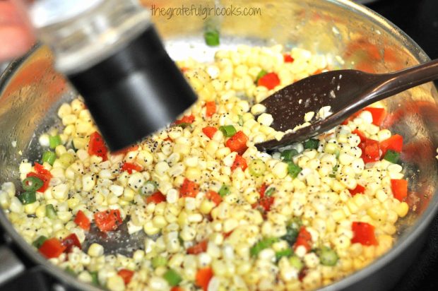 Salt and pepper are added to corn, peppers and green onions
