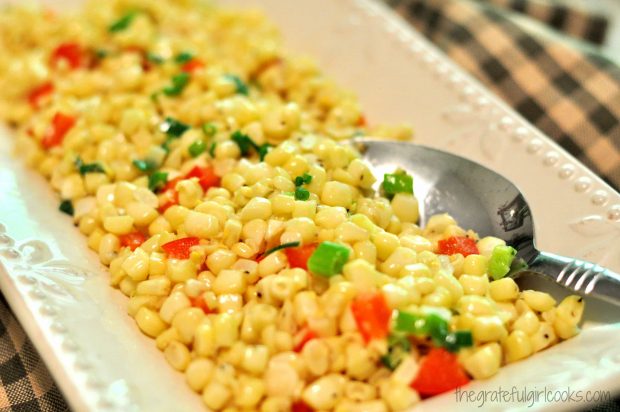 Corn, with red peppers and green onions on serving platter with spoon