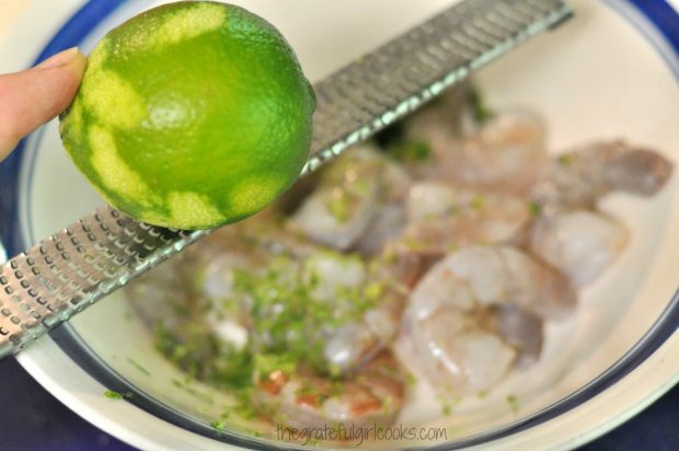 Lime zest is added to the raw shrimp in bowl.