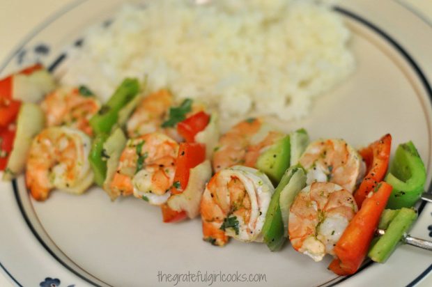 Grilled shrimp kabobs on a plate with rice on the side.