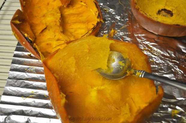 Tender baked pumpkin flesh is removed from shell with a spoon to make pumpkin puree.