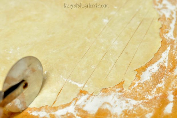 A pizza cutter is used to slice dough for dumplings into thin strips