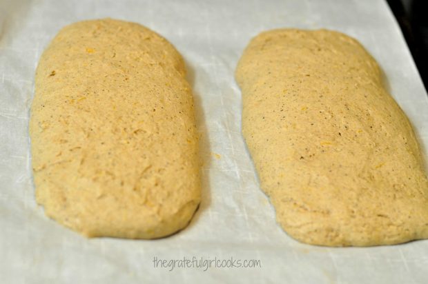 After baking, the biscotti dough has spread considerably, and cools on parchment paper.