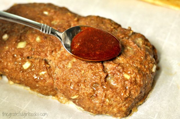 BBQ sauce is spooned over half-baked meatloaf.