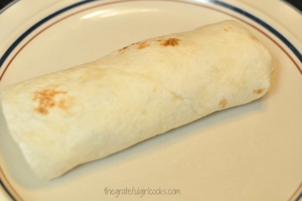 One of the breakfast burritos, rolled up, on a plate.