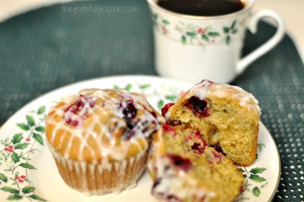 Two cranberry orange muffins on a plate, with a cup of coffee on the side.