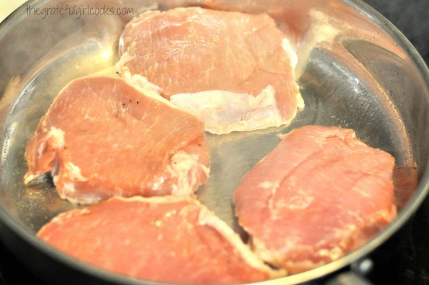 Pork chops are cooked in oil in a hot skillet.