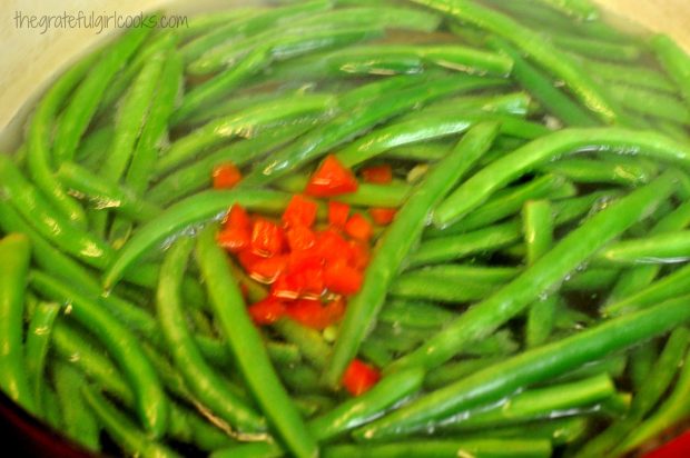 Chopped red bell pepper is added to green beans in water and cooked for one minute.