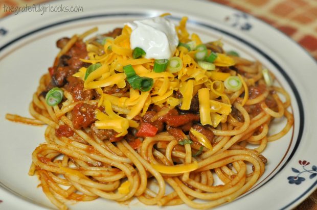 Chili spaghetti is garnished with cheddar cheese, green onions and sour cream before serving.