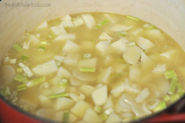 The pot of creamy potato leek soup cooks and the potatoes soften.