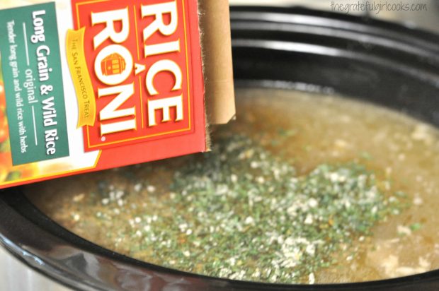 Rice and seasonings are added to slow cooker full of creamy turkey wild rice soup.