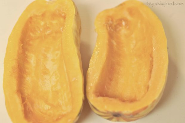 Delicata squash are cut in half and seeds removed before being roasted.