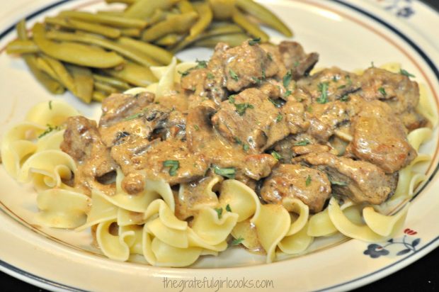 Beef stroganoff served on noodles, with green beans on plate 