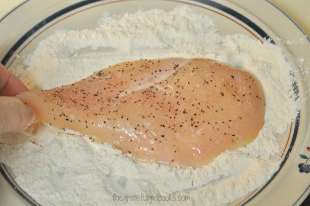 Dredging chicken cutlets in flour and seasonings before cooking.