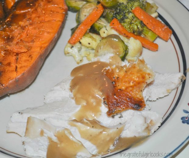 Sliced roast turkey breast is served with gravy, and vegetables on the side.