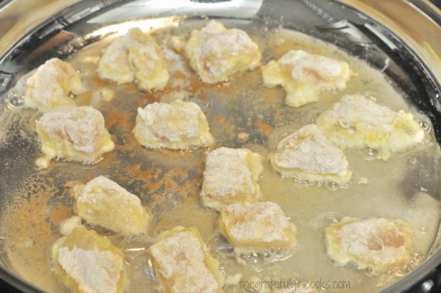 Chicken pieces (for sweet fire chicken) are cooked in hot oil in a large skillet in batches.