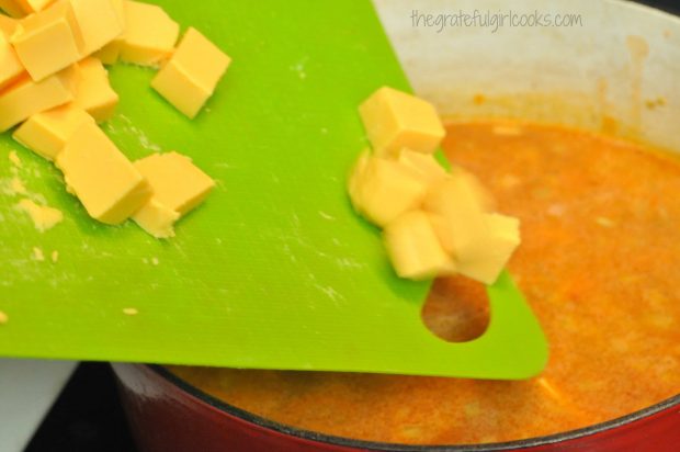 Cheese cubes added to chicken enchilada soup in pan.