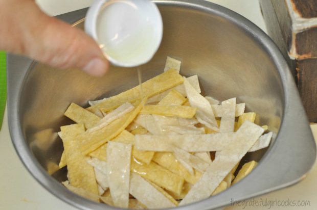 Oil being added to sliced tortilla strips before baking, for chicken enchilada soup garnish