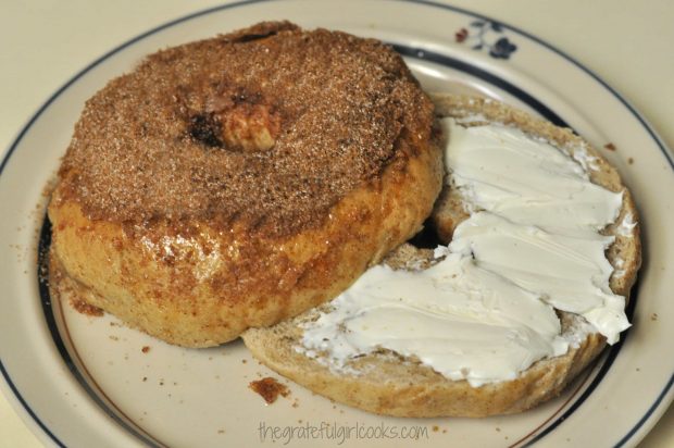 A cinnamon crunch bagel, sliced and topped with cream cheese, on a plate.